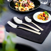 Three-piece cutlery set placed on black table with pasta dish and appetizer in stylish presentation.
